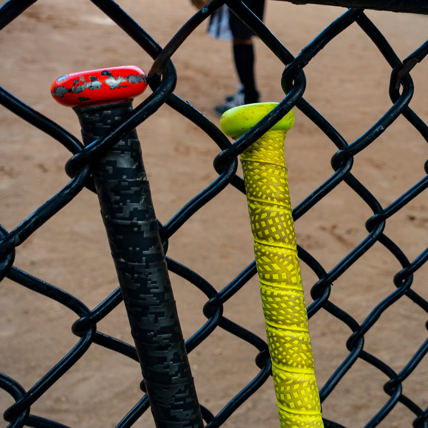 Red and black baseball bat and yellow baseball bat interlocked between chain link fence